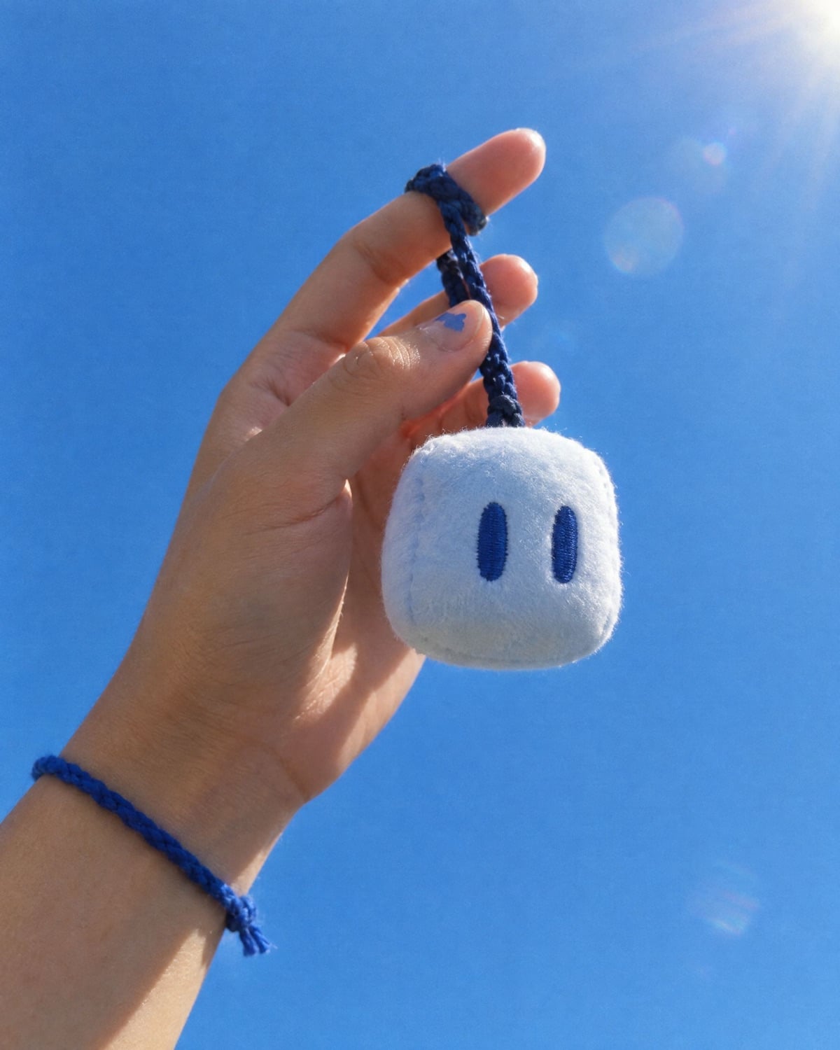 A hand holding a small Pip charm up against a blue sky